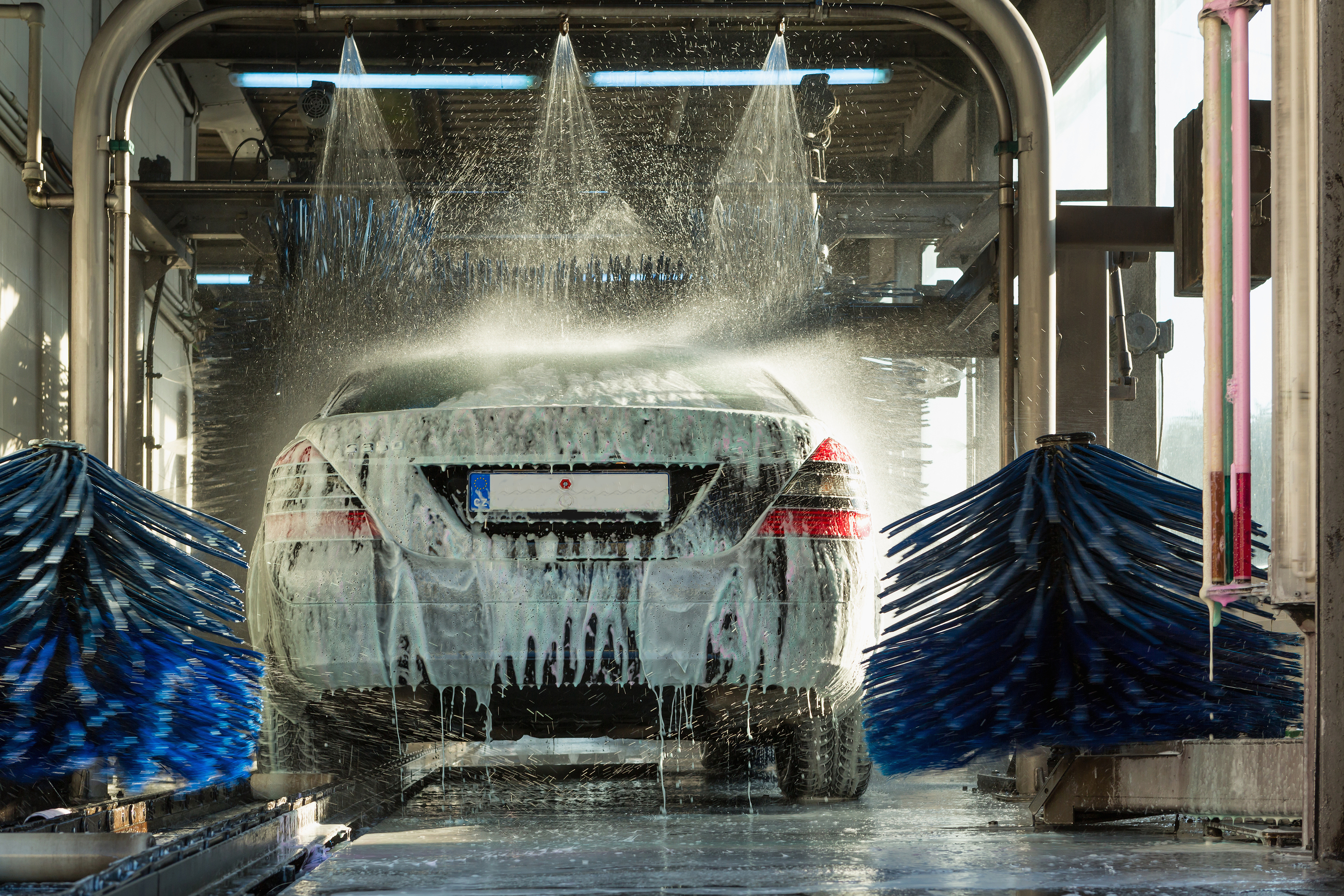a car being washed in a car wash with two blue spinning brushes on each side and three water sprays over it