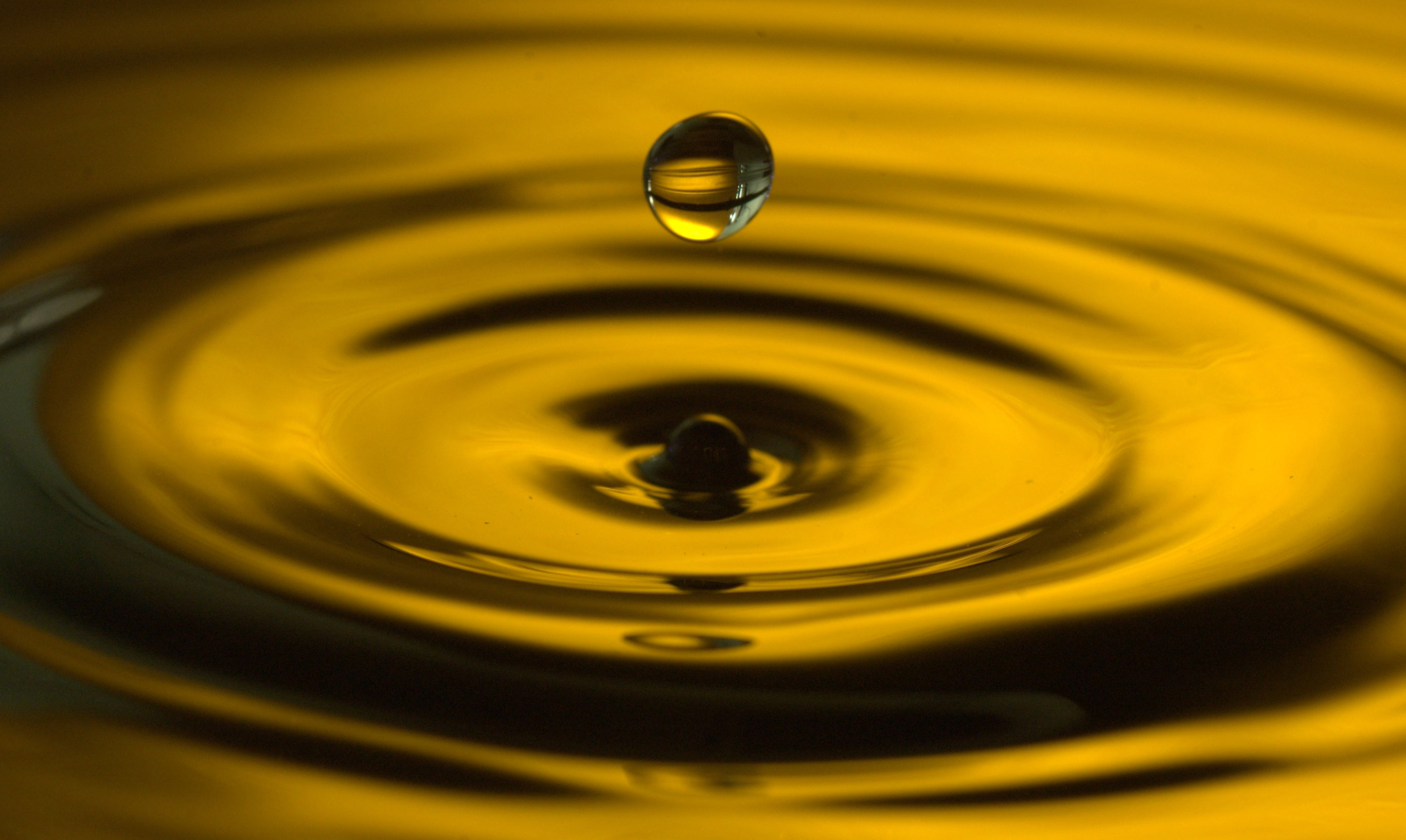 Капля масла растекается по поверхности воды. Круги на воде. Капли воды. Желтые воды. Вода фон.